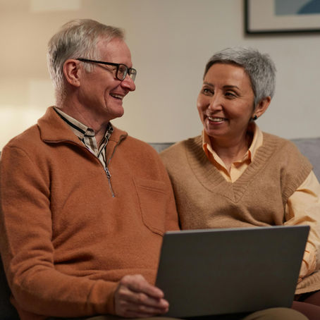Couple sitting together on a couch talking about hormone therapy and health while looking at a laptop