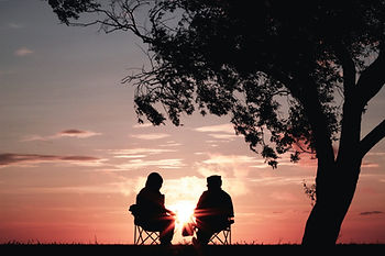 Two people sitting beneath a true at sunset.