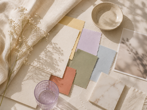 Soft pastel fabric swatches on cream surface, with a delicate plant, marble tile, bowl, and glass, creating a serene and natural mood.