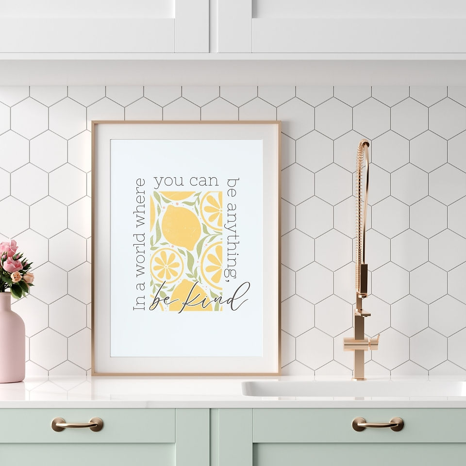 Framed motivational printable with a lemon illustration and the phrase “In a world where you can be anything, be kind,” displayed in a bright modern kitchen.