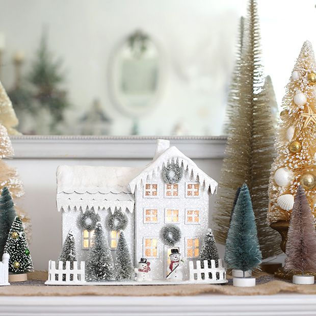 Light-up white Christmas farmhouse with snowy roof, miniature trees, wreaths and glowing windows.