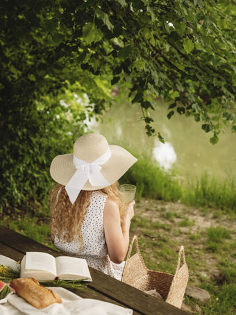woman reading on blanket near trees and pond