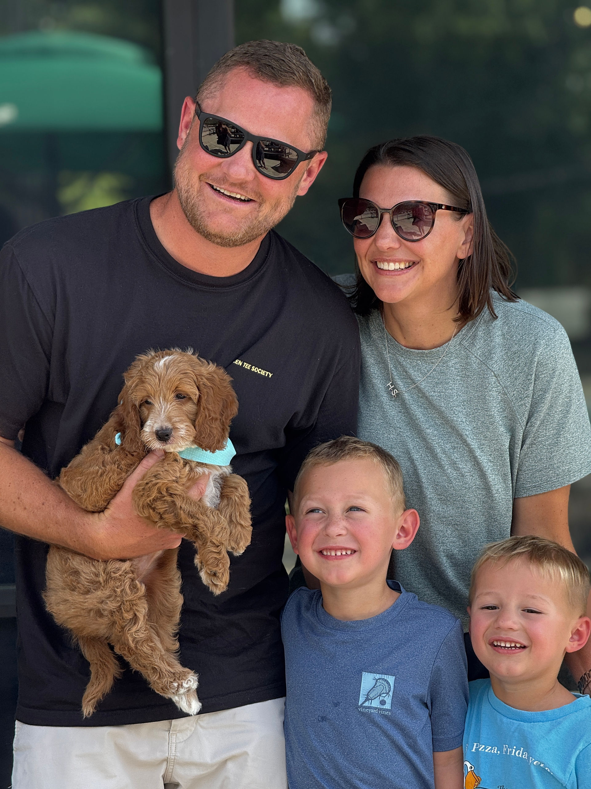 Family of four posing with their new brown curly-coated puppy outdoors.