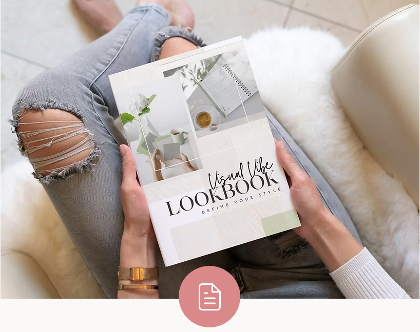 Person in ripped jeans holds a Visual Vibe LOOKBOOK magazine on a beige couch with a white throw.
