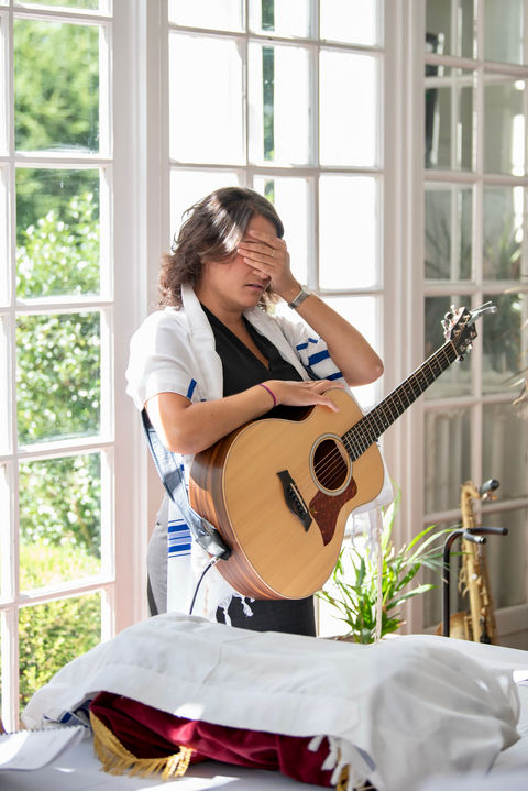 Cantor Stein holding her guitar and covering her eyes at an event in The Hamptons, New York