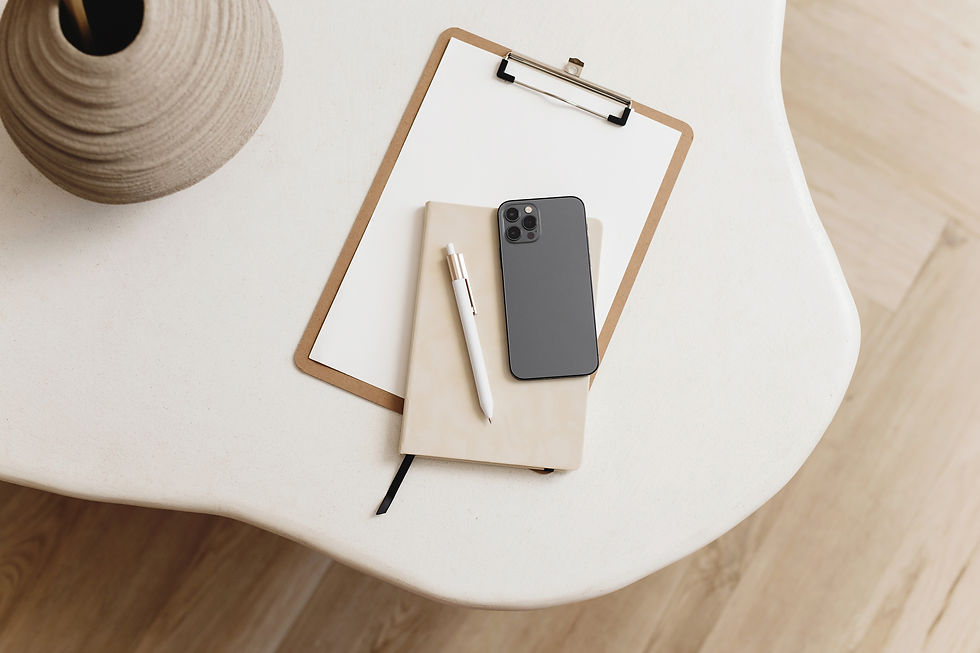 Clipboard, notebook, pen, and smartphone on a white table. Beige vase nearby. Minimalist setting with natural wood floor background.