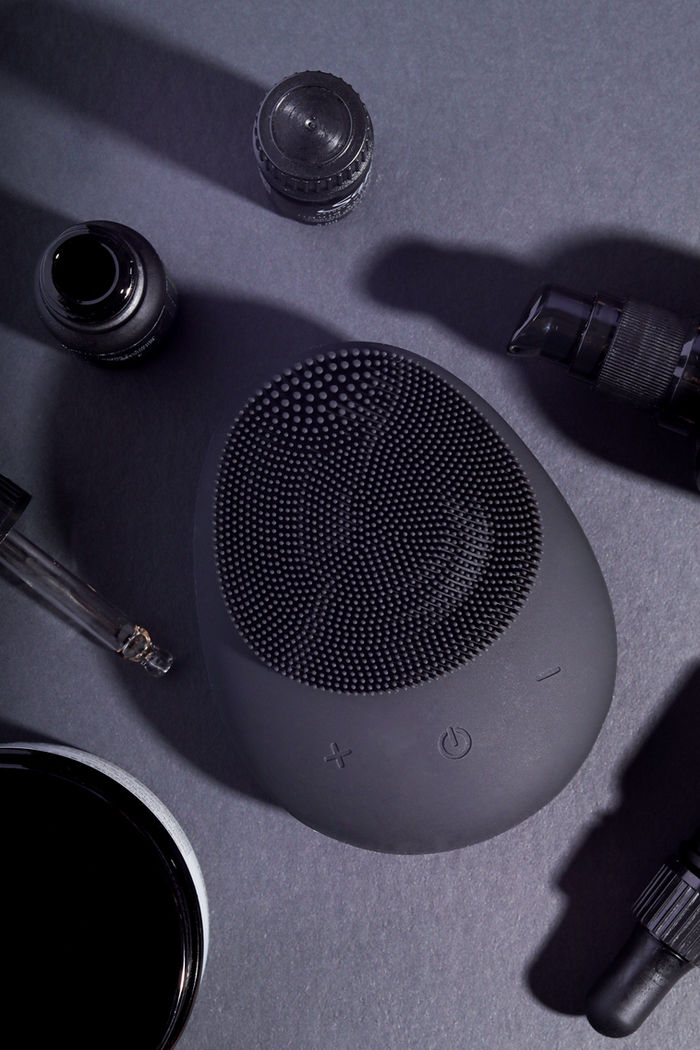 Flat lay photo of black beauty products including a silicone facial scrubber and various facial oils