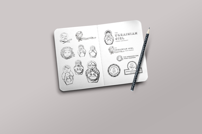 Various sketches of a Ukrainian nesting doll logo design on an open notebook with pencil.