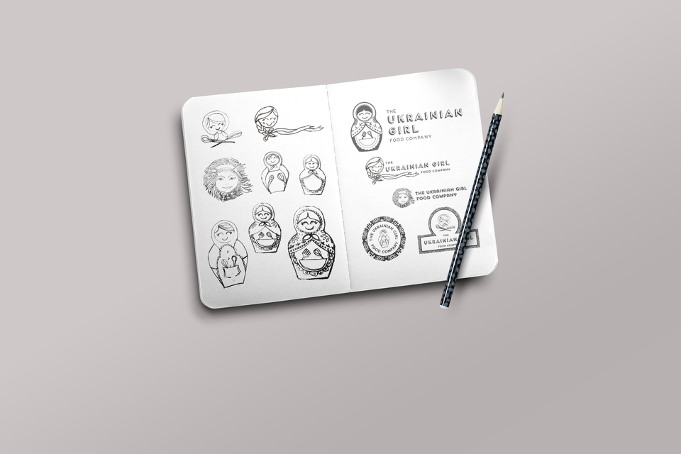 Various sketches of a Ukrainian nesting doll logo design on an open notebook with pencil.