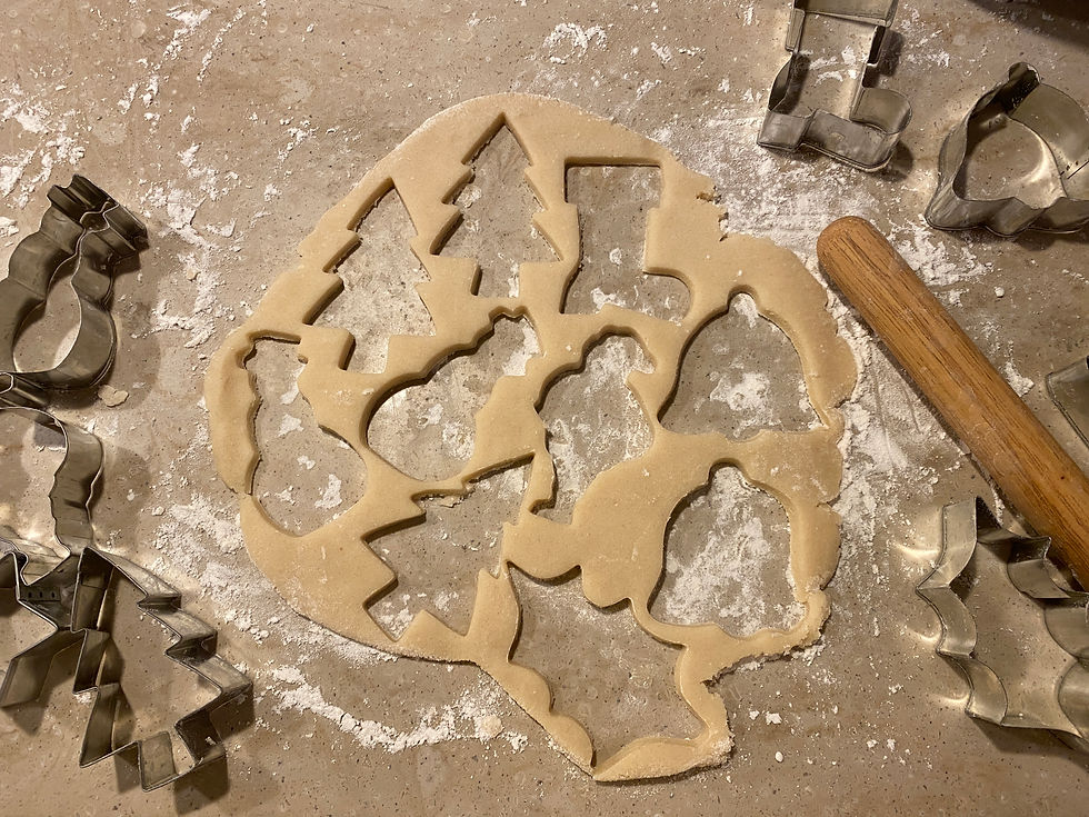 Outline of cut out cookie dough surrounded by cookie cutters and a rolling pin on a surface covered with flour.