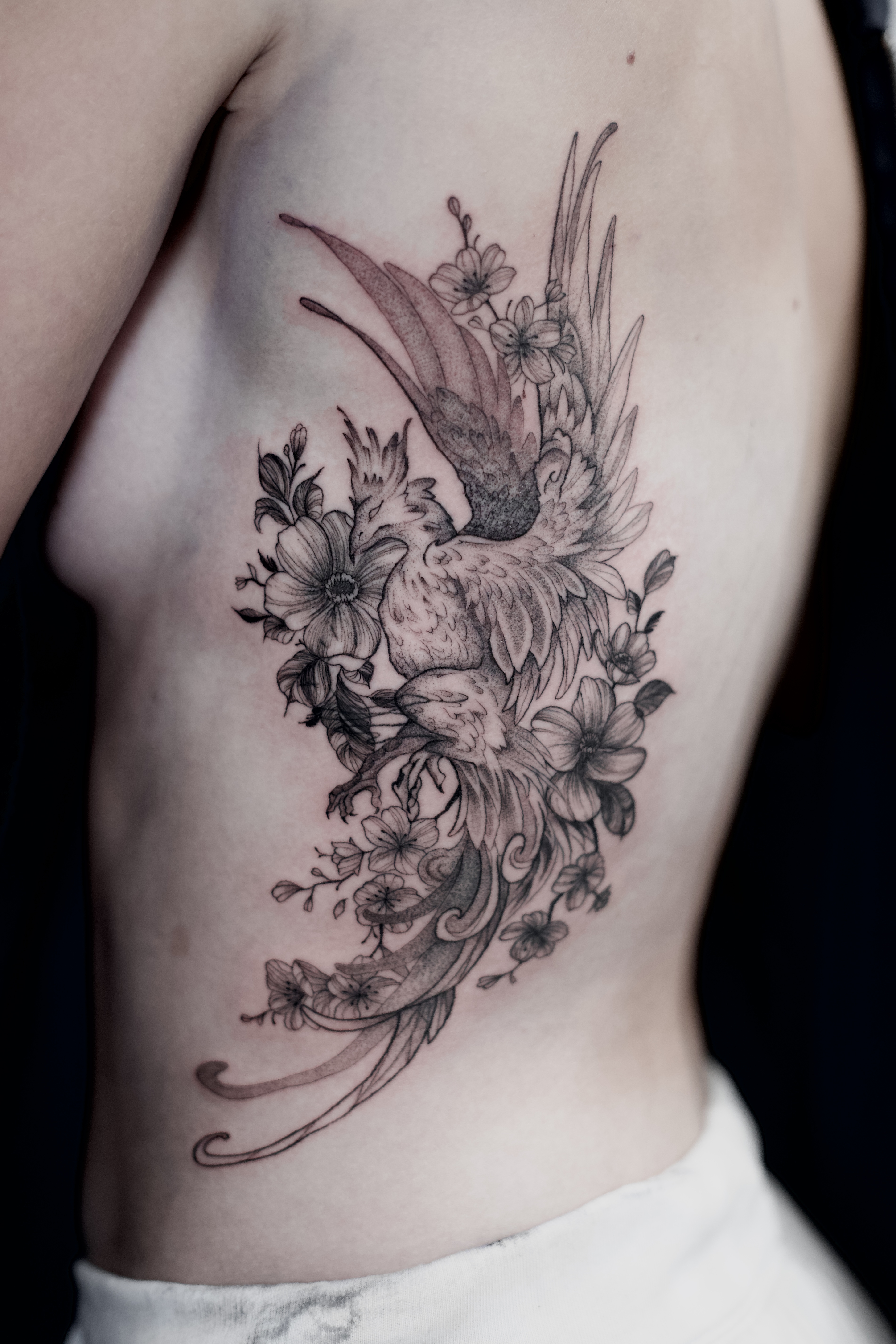 Fine-line phoenix or bird tattoo with flowers along the side and back