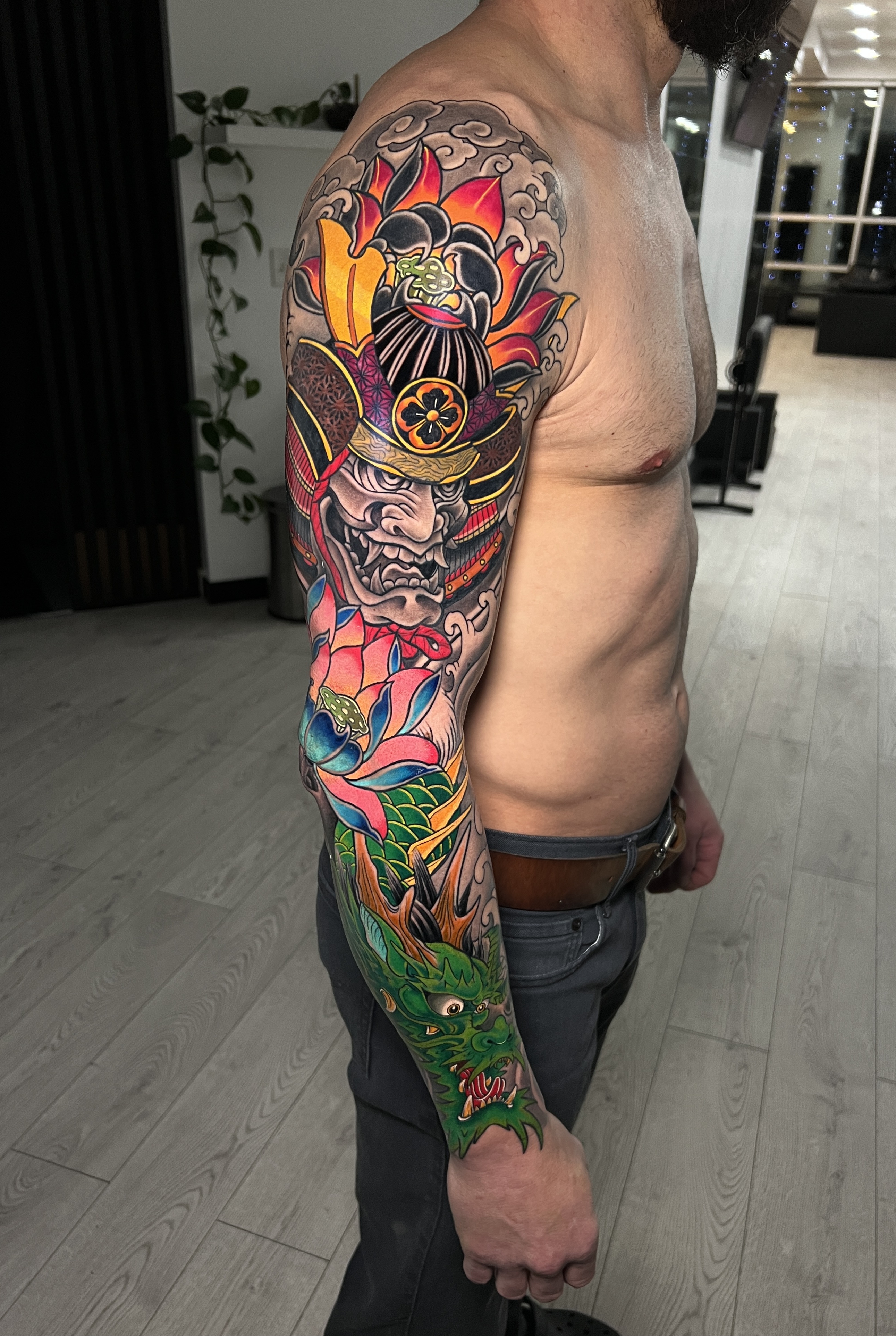 Vivid Japanese and neo-traditional full-arm sleeve with a masked armoured face, flowers, and green and red accents