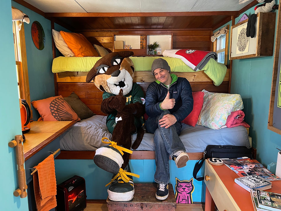A catamount mascot and a man sit on a couch giving a thumbs up.
