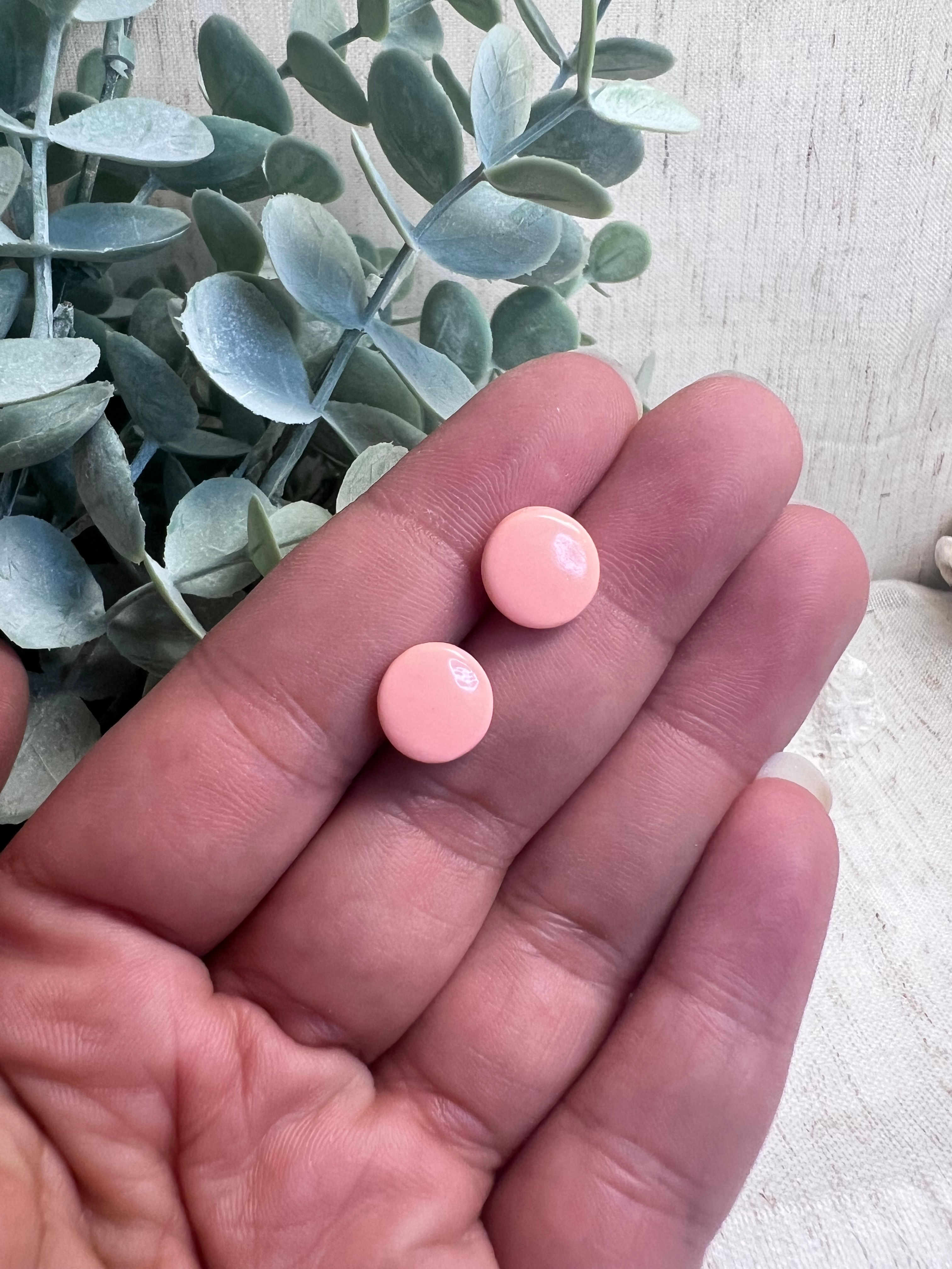 Deux petites boucles d'oreilles roses à la main.