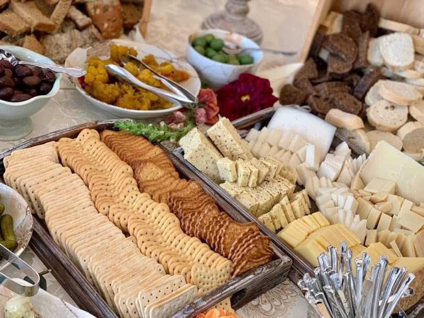 Assorted crackers, cheese, and bread on a buffet table with olives, pickles, and mustard. Elegant table setting with a floral accent.