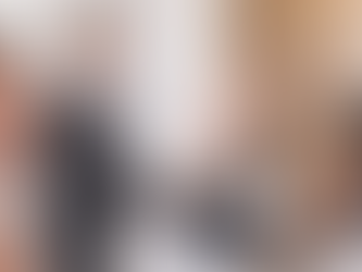 A man seated at a table adds hot sauce to a dish held by a server. White and black table setting, elegant room, wooden floor, guests in the background.