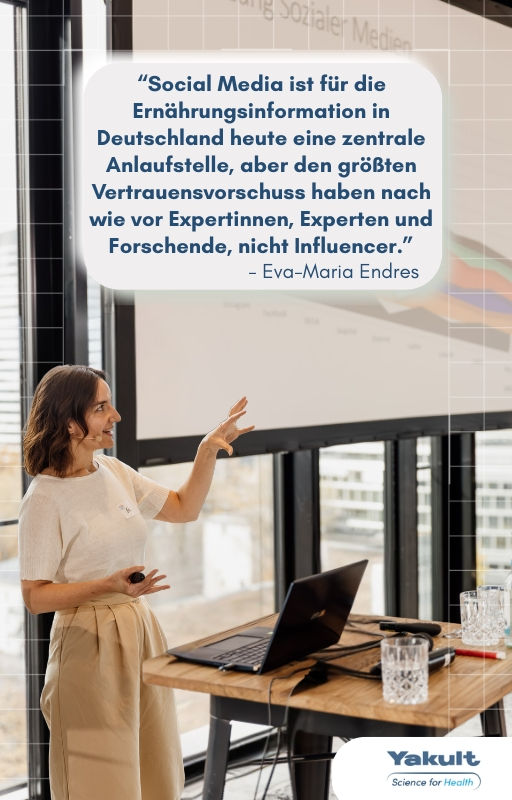 Eva-Maria Endres hält einen Vortrag beim Yakult Science meets Social Media Event: „Social Media ist für die Ernährungsinformation in Deutschland heute eine zentrale Anlaufstelle, aber den großen Vertrauensvorschuss haben nach wie vor Experten und Forschende, nicht Influencern.“ Sie steht vor einer Leinwand, trägt helles Outfit, vor Schreibtisch mit Laptop.