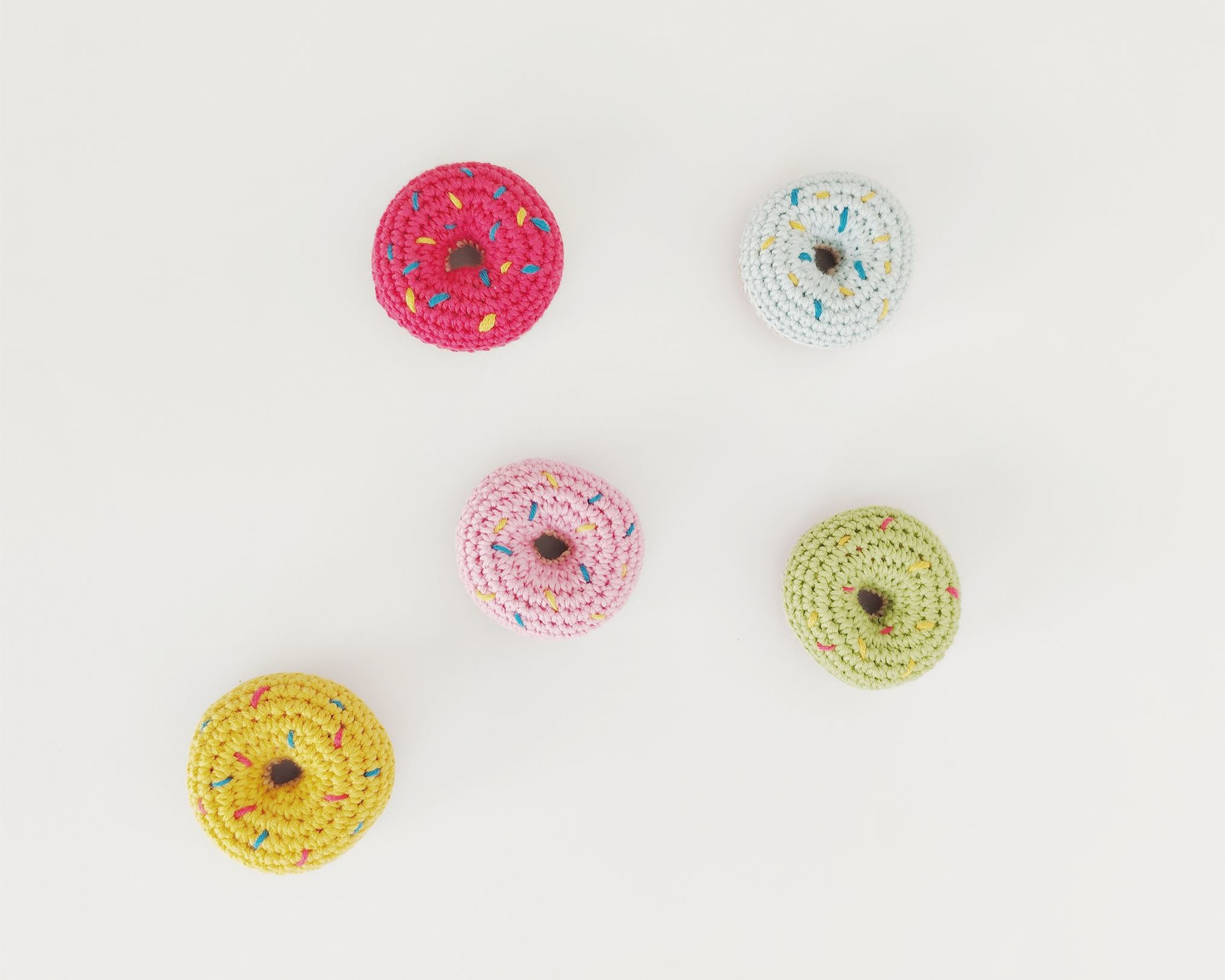 Four colorful donuts. Pink, yellow, green and blue donuts. Ninots on white surface.