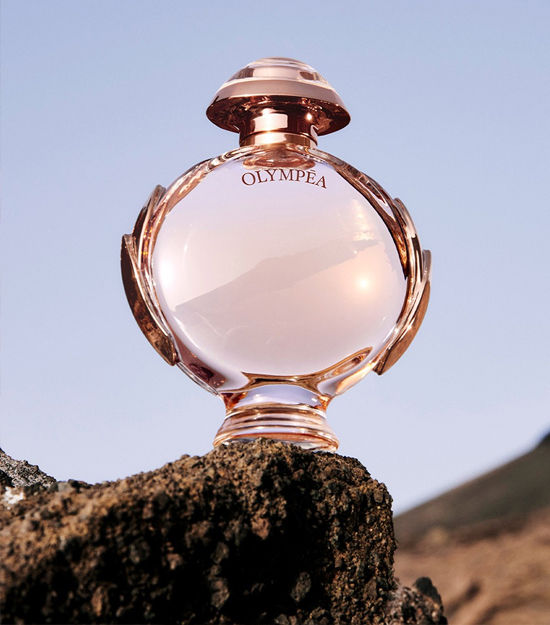 Miniatura: Frasco do perfume Feminino Olympéa EDP de Paco Rabanne em cima de uma pedra ao fundo o céus azul