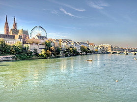 panoramic view of Basel Minster and the Ferris Wheel of the Basel autumn fair, set against the Rhine River, reflecting the city's blend of historical significance and modern vitality, representative of the innovative solutions provided by an interim management company