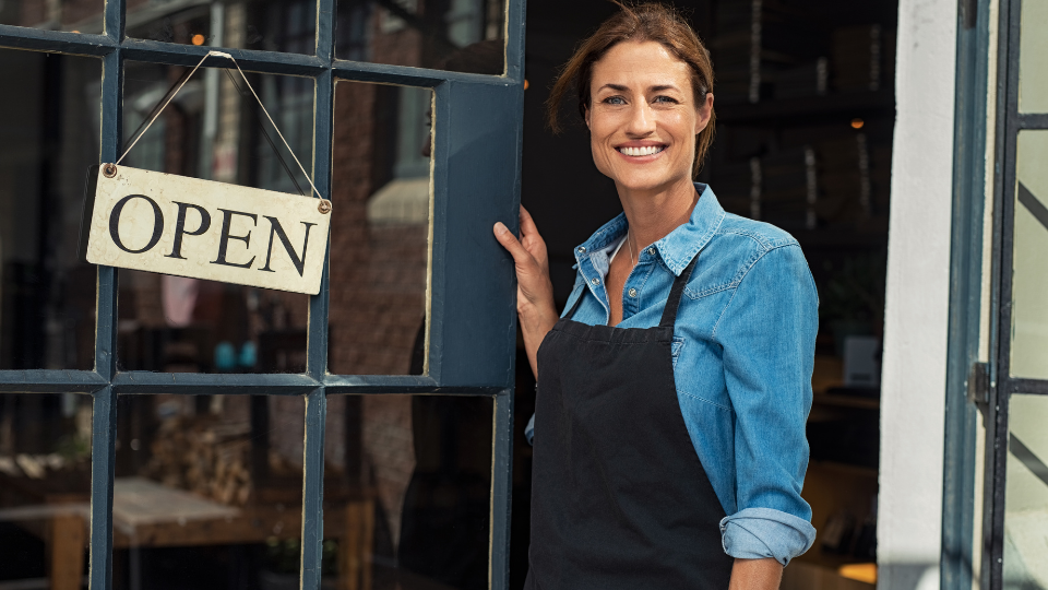Female business owner smiling outside shop with open sign