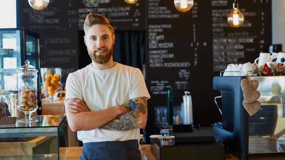 Hip business owner with tattoos standing at counter of coffee shop