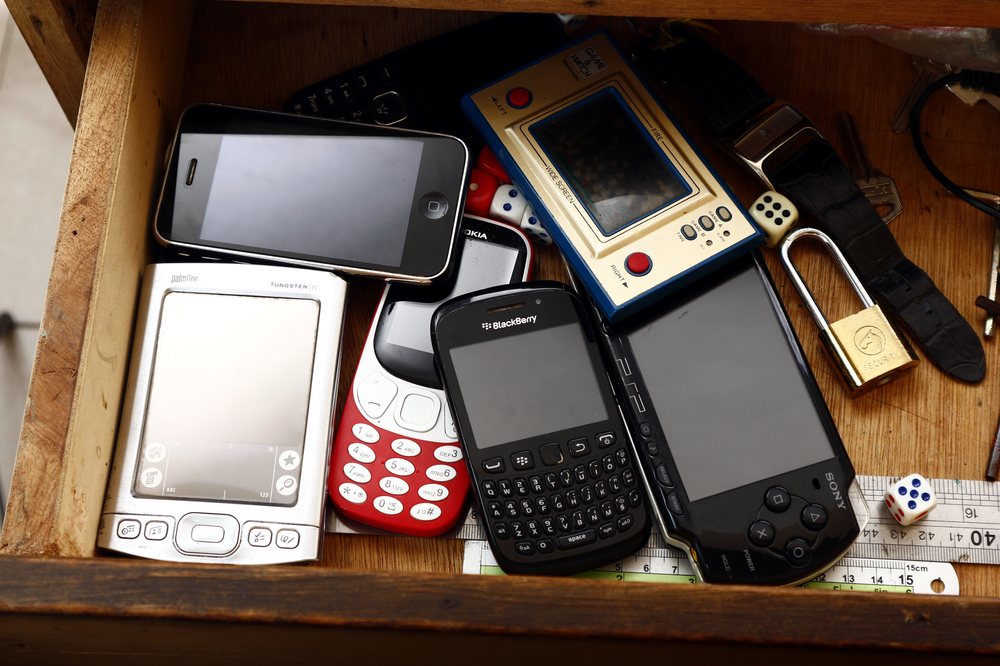 wooden drawer containing old and unused electronic devices like cell phones and personal gaming devices