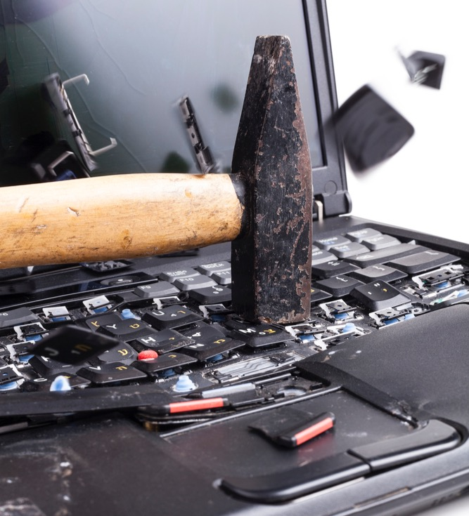 image of a laptop being smashed by a hammer, with parts shattering in pieces