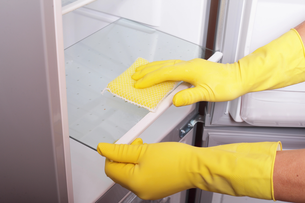 a person wearing gloves and deep cleaning a refrigerator
