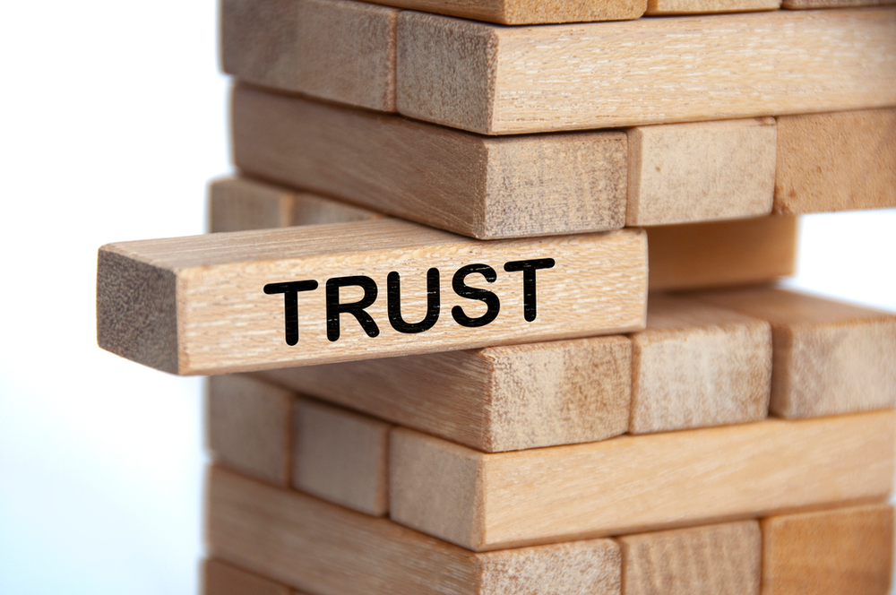 Jenga game with a stick with the word "Trust" being slid out of the puzzle