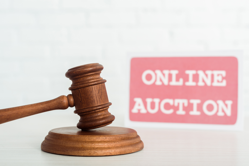 a wooden gavel in the foreground with a blurred sign that says "Online Auction" in the background