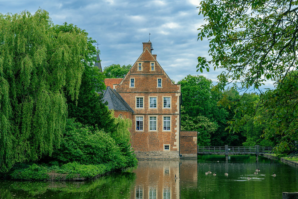 Burg Hülshoff mit der angrenzenden Kapelle umgeben von einem Wassergraben und einer grünen Gartenlandschaft.