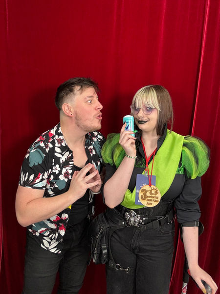 2 people looking at deodorant: A person with green sleeves, and a sash, and Thomas Sanders.