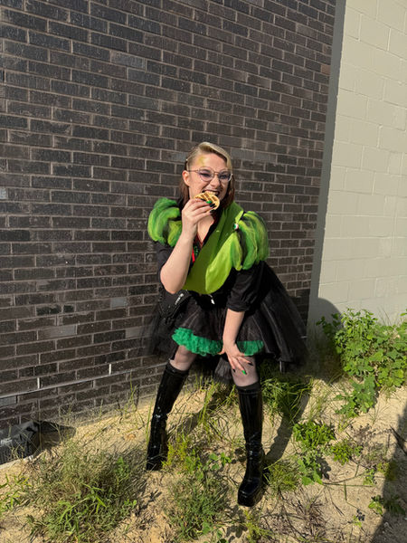 A person with Puffy green sleeves and a sash biting into a wooden third place metal, leaning foreword towards the camera.