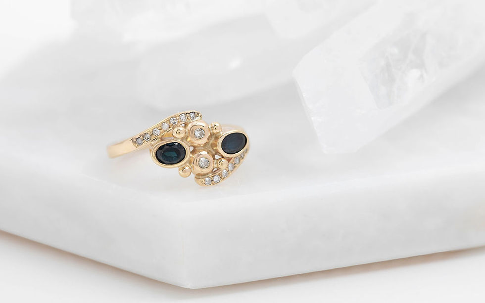 The completed engagement ring, remodelled from two sentimental engagement rings. It features two oval sapphires and two round diamonds in the central setting, with pavé-set diamonds along both arms of the ring shank, all set in 9ct yellow gold.