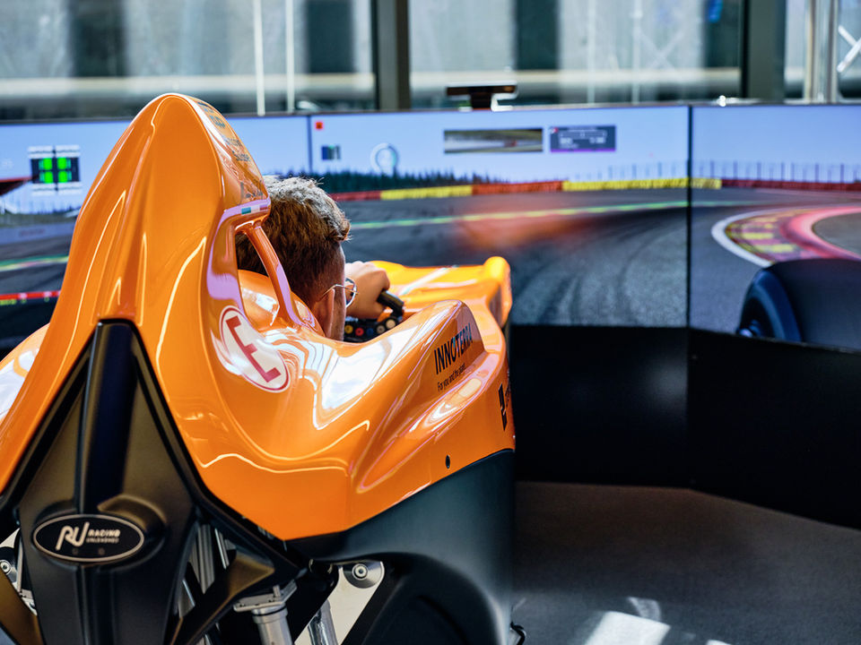 Fahrer in orangem Simulator bei virtuellem Rennen auf Bildschirm-Rennstrecke