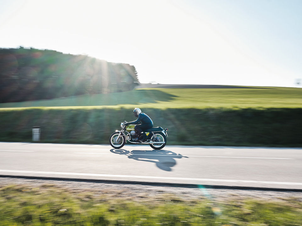 Motorradfahrer fährt durch lichtdurchflutete Landschaft auf einem grünen Motorrad mit schwarzen Ledersitz und Chromteilen