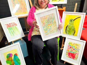 Huong, artist, sitting down with a bunch of her colourful artworks