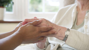 Older person's hands that have tendinitis, held gently by another in a comforting gesture. Bright room with a window in the background. Peaceful mood.