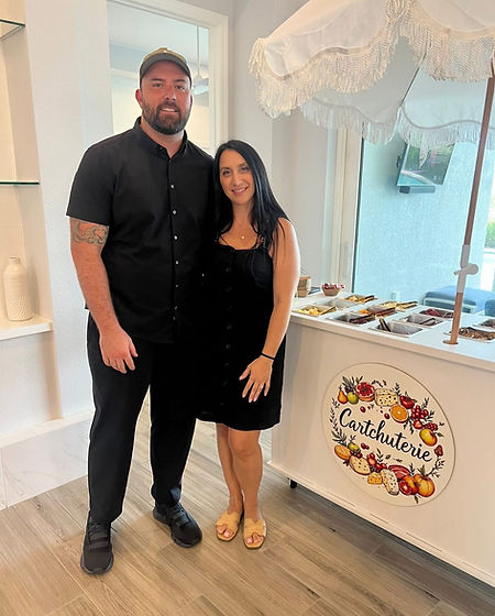 Michael Dailey and Annmarie Tuohy, co-founders of Cartchuterie, standing together with their custom charcuterie cart, smiling