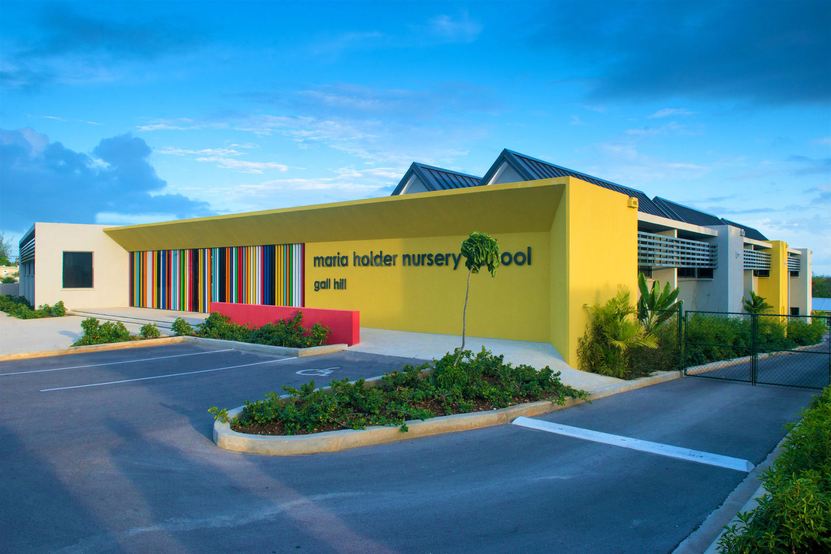 Maria Holder Nursery School
Gall Hill
Barbados
The first school to be completed in the Maria Holder Memorial Trust nursery school series, is this 150 pupil school for 3 to 5 year olds.
Located in a residential neighbourhood, the size of the school is deceptive. Designed to blend with the scale of the surrounding houses the school sits comfortably within the sloping topography of the site; single storey at the front and two storey to the rear.
Set around a secure cloistered courtyard, single bay classrooms promote breezy naturally ventilated learning spaces. Classrooms dialogue with each other and with the courtyard through large openings and windows allowing transparency and reducing hidden spaces to promote child security.
Blending the Barbadian chattel house vernacular with a distinctive, colourful, contemporary aesthetic, the school’s architecture is both familiar and progressive and reflects our aim to provide a safe, child-centred environment where children want to be.