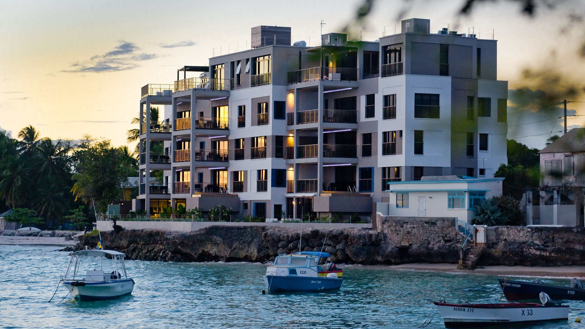Ocean Reef
Barbados
The architecture of this 12 unit luxury condominium offers spacious contemporary accommodation which is both informed by and exploits an incredible location.
Built on a narrow cliff site over looking a bay on the island’s south coast, the building’s form mirrors the curved edge of the land in order to optimise views and overcome the density challenges of the brief.
Modern open plan living spaces with large floor to ceiling, wall to wall glass sliding doors open onto generous covered terraces and panoramic sea views. There are private plunge pools incorporated into first floor and junior penthouse units and a roof top swimming pool in the main penthouse to exploit the advantages of outdoor tropical living.
The façade’s articulation produces an architectural language which is human in scale and modern while maintaining unmistakably Caribbean threads.