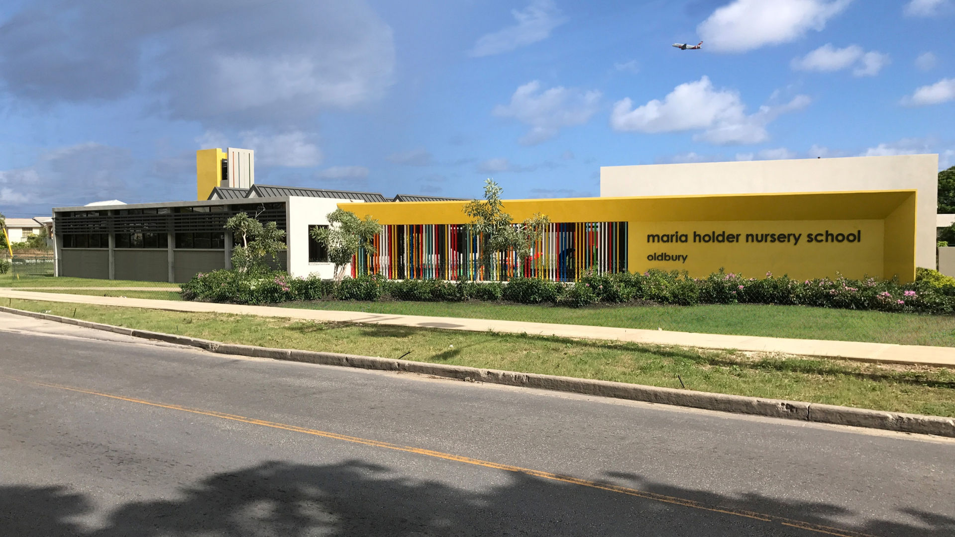 Maria Holder Nursery School
Oldbury
Barbados
The second school to be completed in the Maria Holder Memorial Trust nursery school series is this 90 pupil school for 3-5 year olds.
The school is located on an arterial road near to the airport and opposite a grove of mahogany trees. Designed to blend with the scale of the surrounding houses the building sits comfortably within of the site taking advantage of its proximity to the majestic trees that are clearly visible from inside the school.
Set around a secure cloistered courtyard, single bay classrooms
promote breezy naturally ventilated learning spaces. Classrooms dialogue with each other and with the courtyard through large openings and windows allowing transparency and reducing hidden spaces to promote child security.
Blending the Barbadian chattel house vernacular with a distinctive, colourful, contemporary aesthetic, the school’s architecture is both familiar and progressive and reflects our aim to provide a safe, child-centred environment where children want to be.
