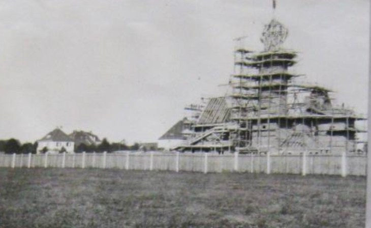 Der Rohbau der Kirche auf freiem Feld, Turm und Dachstuhl sind von einem Hölzergerüst umgeben.