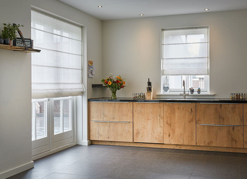 Wooden kitchen with light gray floor, two windows with white blinds, vase of flowers on counter, knife set, and small plants on shelf.
