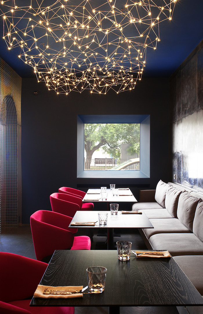 Luxury restaurant interior in Sydney with a dark moody atmosphere, red velvet chairs, banquette seating, and sculptural lighting