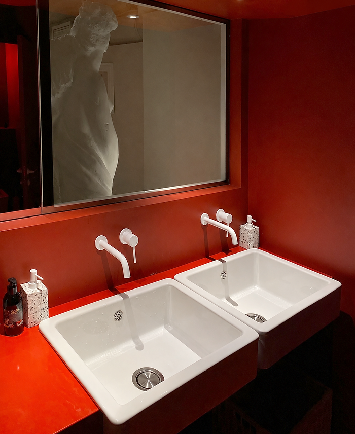 Cafe bathroom interior design Sydney with red walls, white tapware and sculptural mirror reflection by AZAR