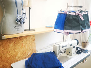 Sewing room with industrial sewing machine, a pile of folded clothes and redesigned shorts on hangers.