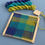 Thumbnail: square frame loom weaving kit with woven example in blue green and turquoise yarn