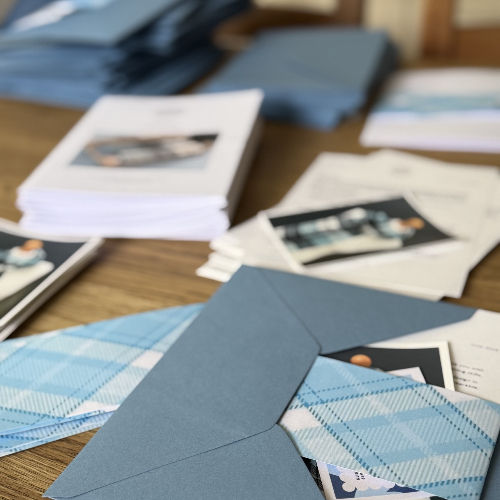Stacks of blue patterned envelopes and printed cards spread across a wooden table, suggesting invitation assembly.